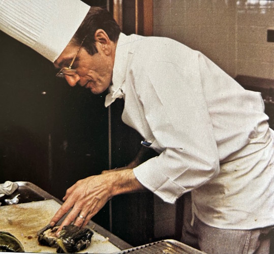 A person in a chef's uniform cutting fish.